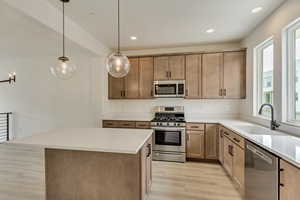 Kitchen featuring sink, appliances with stainless steel finishes, light hardwood / wood-style flooring, a kitchen island, and pendant lighting