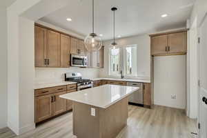 Kitchen featuring stainless steel appliances, sink, light wood-type flooring, pendant lighting, and a center island