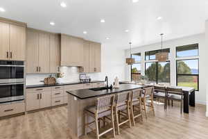 Kitchen featuring light brown cabinetry, stainless steel double oven, a kitchen island with sink, recessed lighting, and pendant lighting