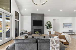 Living area with light wood finished floors, recessed lighting, lofted ceiling, a large fireplace, and french doors