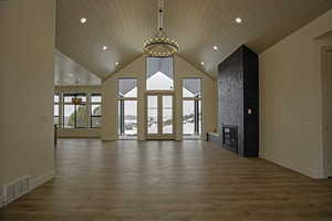 Unfurnished living room with hardwood / wood-style floors, high vaulted ceiling, a fireplace, wooden ceiling, and a chandelier