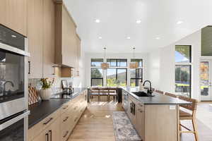 Kitchen featuring dark countertops, light brown cabinetry, stainless steel double oven, a kitchen breakfast bar, and recessed lighting