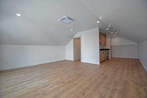 Additional living space with light hardwood / wood-style flooring and vaulted ceiling