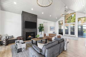 Living room with french doors, high vaulted ceiling, light wood-style floors, recessed lighting, and a large fireplace