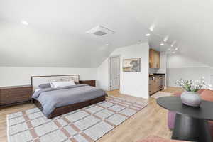 Bedroom featuring light wood finished floors, vaulted ceiling, recessed lighting, and beverage cooler