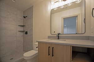 Bathroom featuring vanity, tiled shower, and toilet