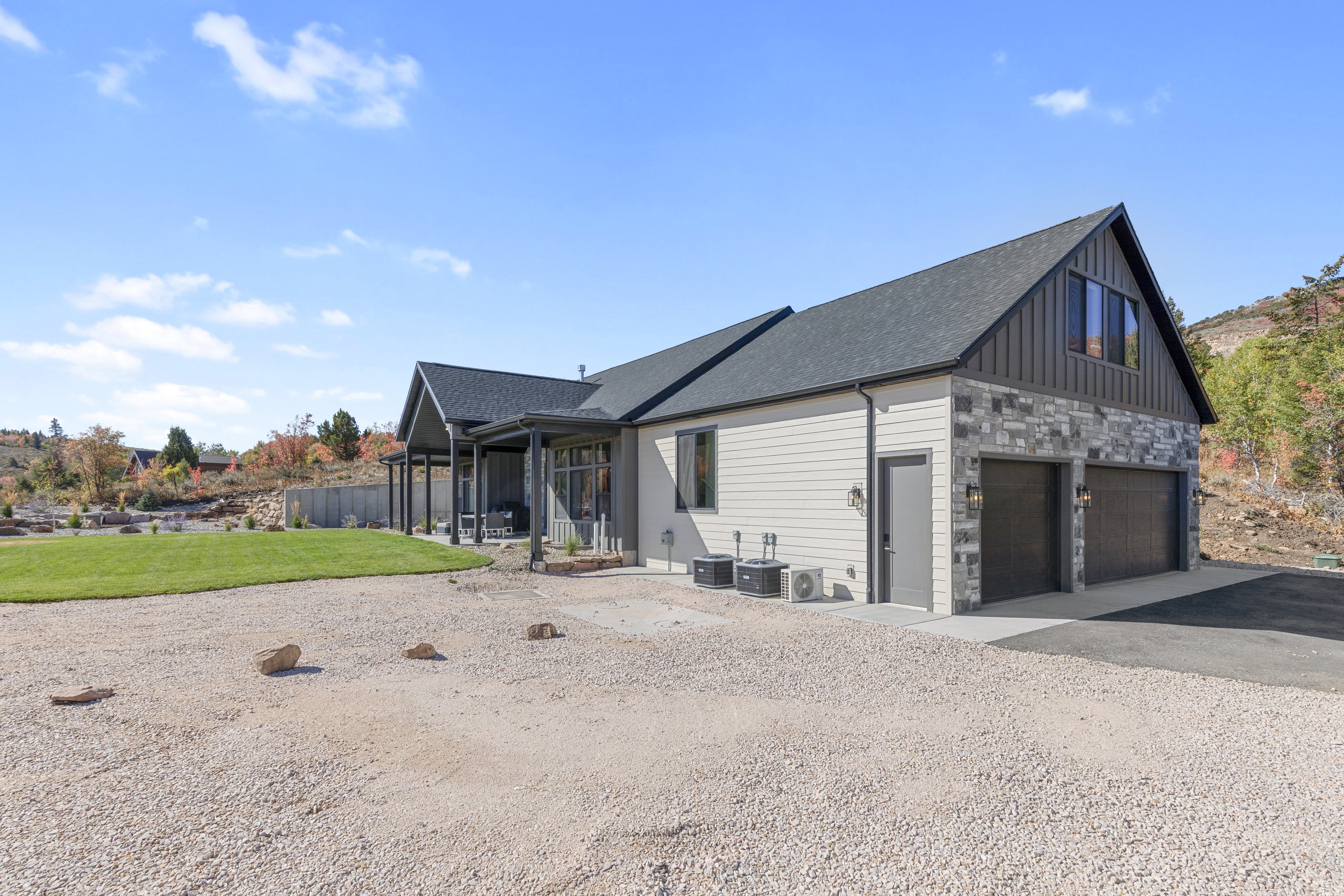 View of side of home featuring a garage, stone siding, a patio, driveway, and board and batten siding
