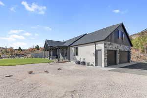 View of side of home featuring a garage, stone siding, a patio, driveway, and board and batten siding