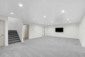 Unfurnished living room with recessed lighting, light colored carpet, and stairway