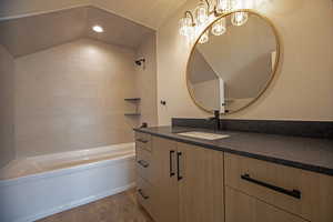 Bathroom featuring hardwood / wood-style flooring, vanity, tiled shower / bath, vaulted ceiling, and a chandelier
