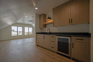 Kitchen featuring lofted ceiling, sink, beverage cooler, light brown cabinets, and light wood-type flooring