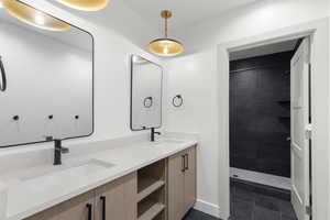 Bathroom featuring double vanity, a tile shower, and dark tile patterned flooring