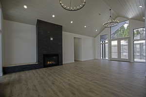 Unfurnished living room with high vaulted ceiling, dark hardwood / wood-style flooring, a chandelier, a tiled fireplace, and french doors