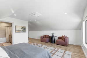 Bedroom with vaulted ceiling, light wood finished floors, recessed lighting, and connected bathroom