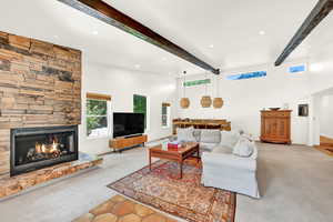 Living room with beam ceiling, a stone fireplace, and light carpet