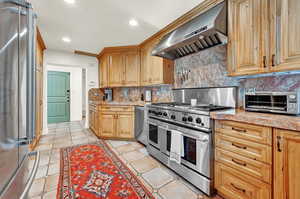 Kitchen with premium appliances, decorative backsplash, light tile patterned floors, and wall chimney exhaust hood