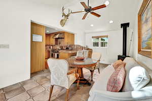 Tiled dining space featuring ceiling fan, vaulted ceiling, and a wood stove