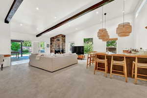 Carpeted living room with high vaulted ceiling, a fireplace, beamed ceiling, and brick wall