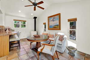 Dining area featuring ceiling fan, light tile patterned floors, a wood stove, and lofted ceiling