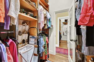 Walk in closet with light hardwood / wood-style floors