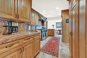 Kitchen with decorative backsplash, wall chimney exhaust hood, sink, range with two ovens, and light tile patterned floors