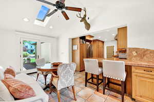 Living room featuring vaulted ceiling with skylight, ceiling fan, and light tile patterned floors