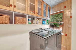 Laundry area featuring tile walls, washing machine and clothes dryer, and cabinets