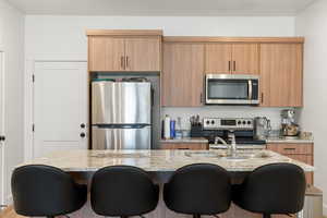 Kitchen featuring a kitchen breakfast bar, light stone countertops, an island with sink, and stainless steel appliances