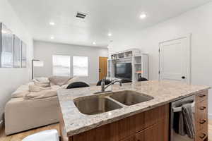 Kitchen with sink, stainless steel dishwasher, light hardwood / wood-style flooring, and light stone counters