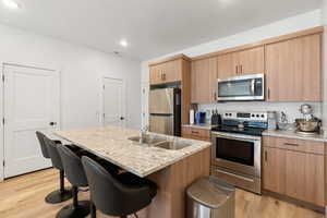 Kitchen with light hardwood / wood-style floors, appliances with stainless steel finishes, sink, and an island with sink