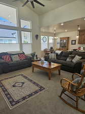 Living room featuring ceiling fan with notable chandelier, high vaulted ceiling, and carpet