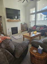 Living room with high vaulted ceiling, ceiling fan, a fireplace, and carpet flooring