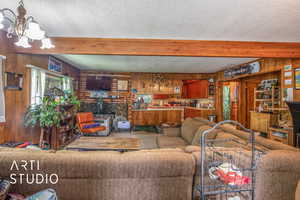 Living room featuring beamed ceiling, an inviting chandelier, a textured ceiling, and wooden walls