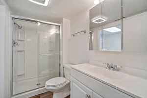 Bathroom with hardwood / wood-style flooring, a shower with door, vanity, and toilet