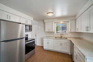 Kitchen with hardwood / wood-style floors, appliances with stainless steel finishes, sink, and white cabinets