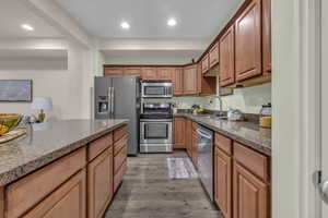 Kitchen with hardwood / wood-style flooring, stainless steel appliances, sink, and dark stone countertops