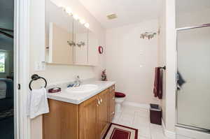 Bathroom with toilet, a shower with door, tile patterned flooring, and vanity