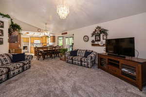 Living room featuring carpet flooring, ceiling fan with notable chandelier, and lofted ceiling