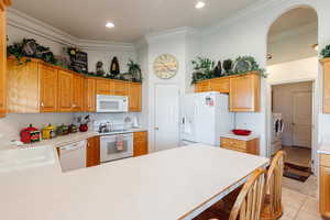 Kitchen with sink, white appliances, light tile patterned floors, crown molding, and kitchen peninsula