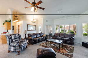 Carpeted living room with ceiling fan with notable chandelier and crown molding