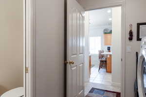 Corridor with ornamental molding, light tile patterned floors, and washer / clothes dryer