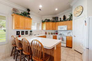 Kitchen featuring a kitchen breakfast bar, ornamental molding, white appliances, light tile patterned floors, and kitchen peninsula