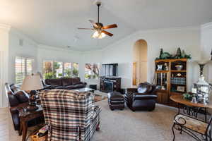 Carpeted living room featuring ceiling fan, crown molding, and lofted ceiling