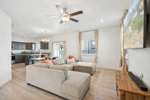 Living room with ceiling fan with notable chandelier and light hardwood / wood-style flooring