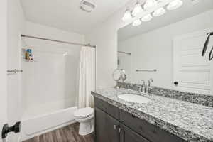 Full bathroom with hardwood / wood-style flooring, vanity, shower / tub combo, and toilet