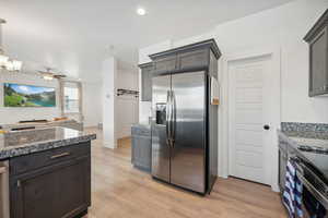 Kitchen featuring stainless steel appliances, ceiling fan with notable chandelier, dark stone countertops, and light wood-type flooring