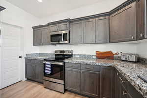 Kitchen featuring light wood-type flooring, stone countertops, and stainless steel appliances