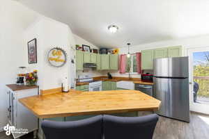 Kitchen with light wood-type flooring, green cabinetry, appliances with stainless steel finishes, sink, and lofted ceiling