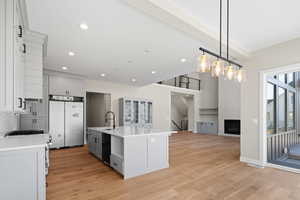 Kitchen featuring dishwasher, high end refrigerator, light hardwood / wood-style floors, an island with sink, and hanging light fixtures