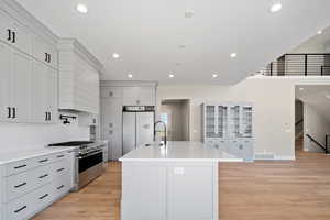 Kitchen with custom range hood, an island with sink, light hardwood / wood-style floors, sink, and high end appliances